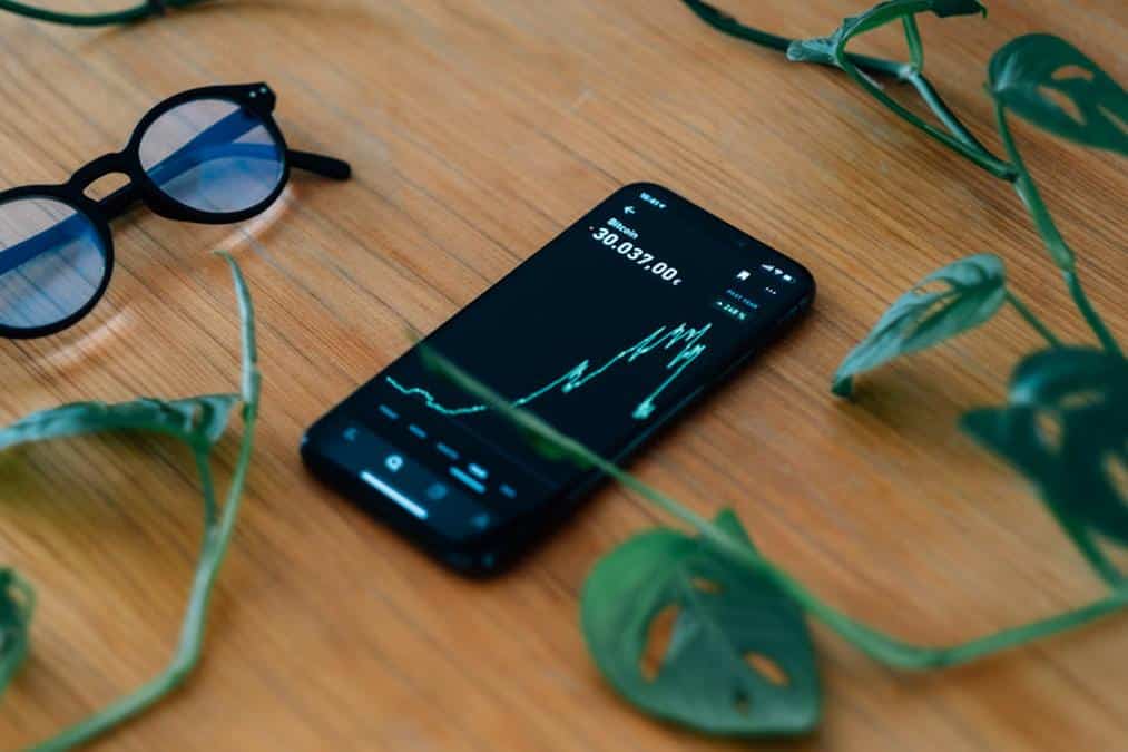 cell phone lays on a wooden table showing a chart - Image of Cryptocurrency, "Cryptocurrency"